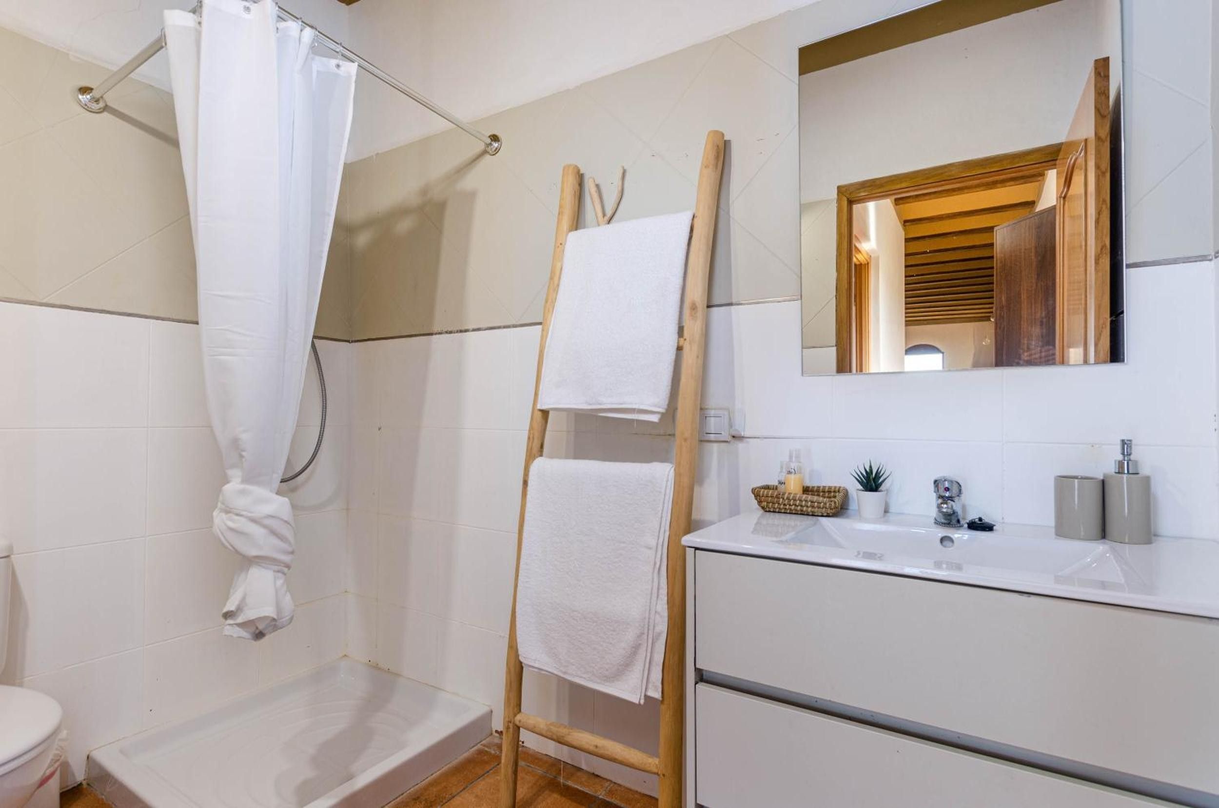 A bathroom with a shower, a wooden towel rack, a sink with toiletries, and a mirror.