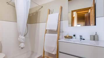 A bathroom with a shower, a wooden towel rack, a sink with toiletries, and a mirror.