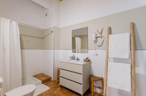 Une salle de bain équipée d’une douche, de toilettes, d’un meuble-lavabo avec miroir et d’un sèche-cheveux fixé au mur.