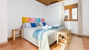 Quarto com cama, duas mesas de cabeceira, janela com cortinas e um ornamento de parede colorido.