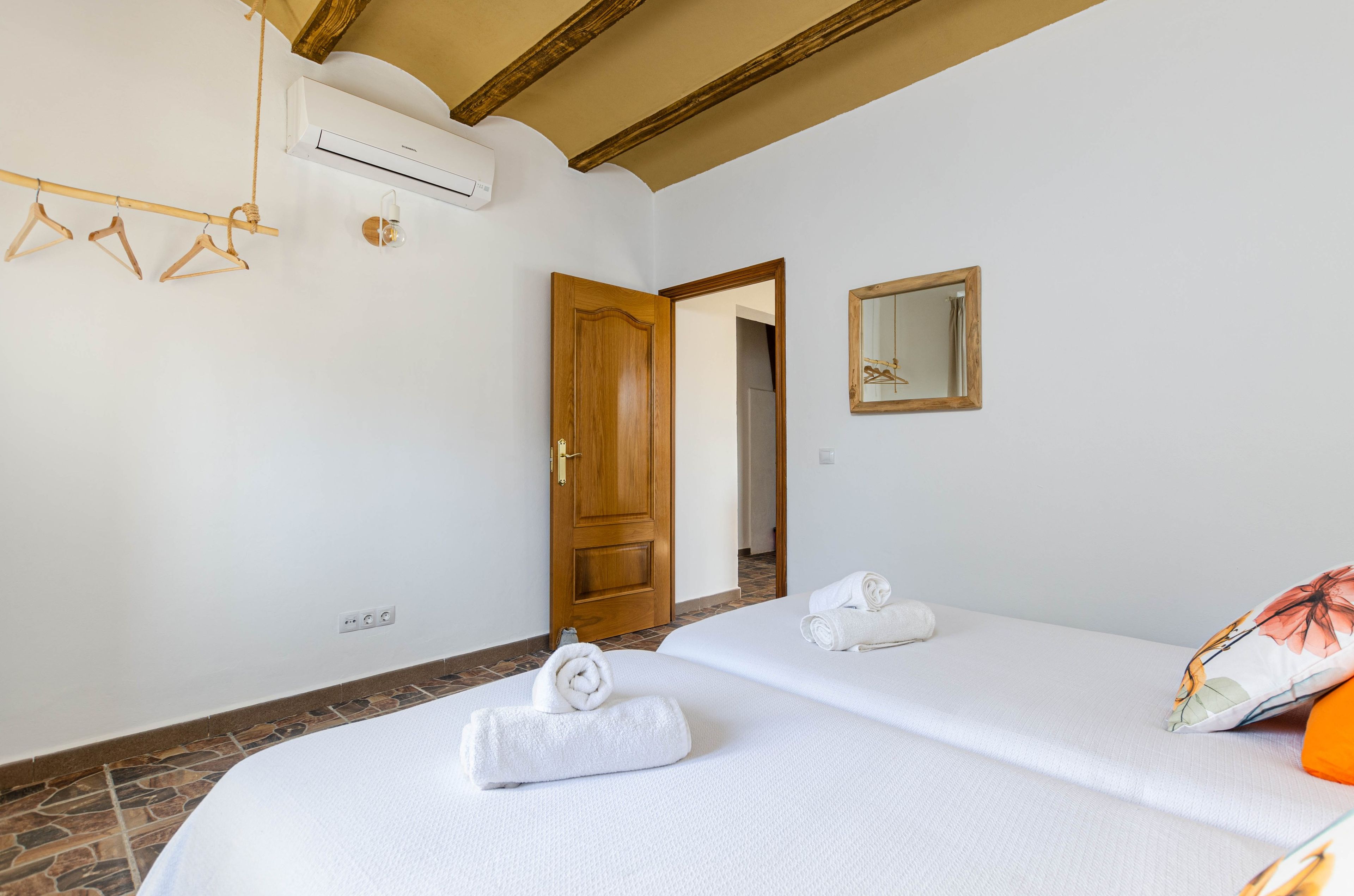 A hotel room with two beds, a wooden door, a mirror, and an air conditioning unit.