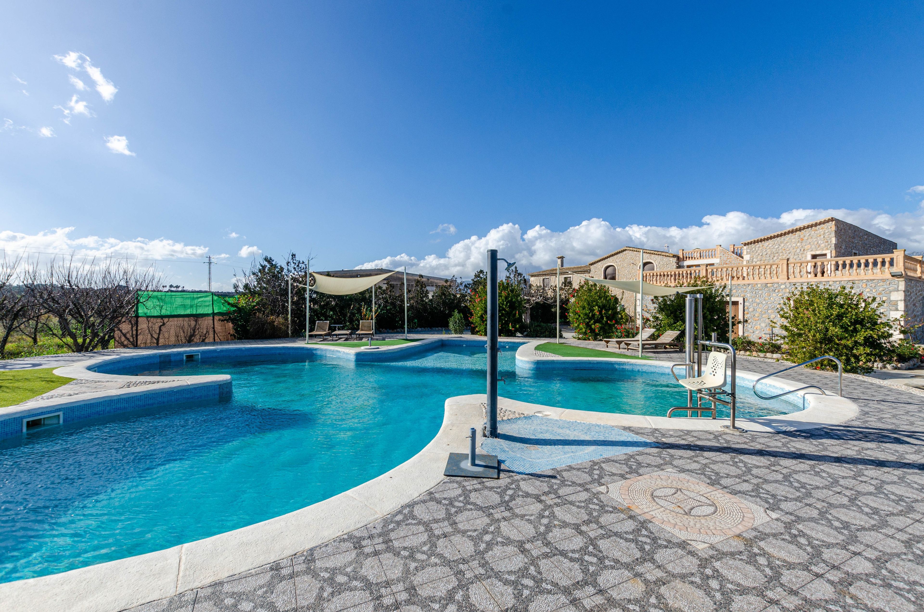 A swimming pool with a curved design, surrounded by a stone patio and a building with a stone facade.
