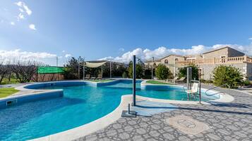 A swimming pool with a curved design, surrounded by a stone patio and a building with a stone facade.