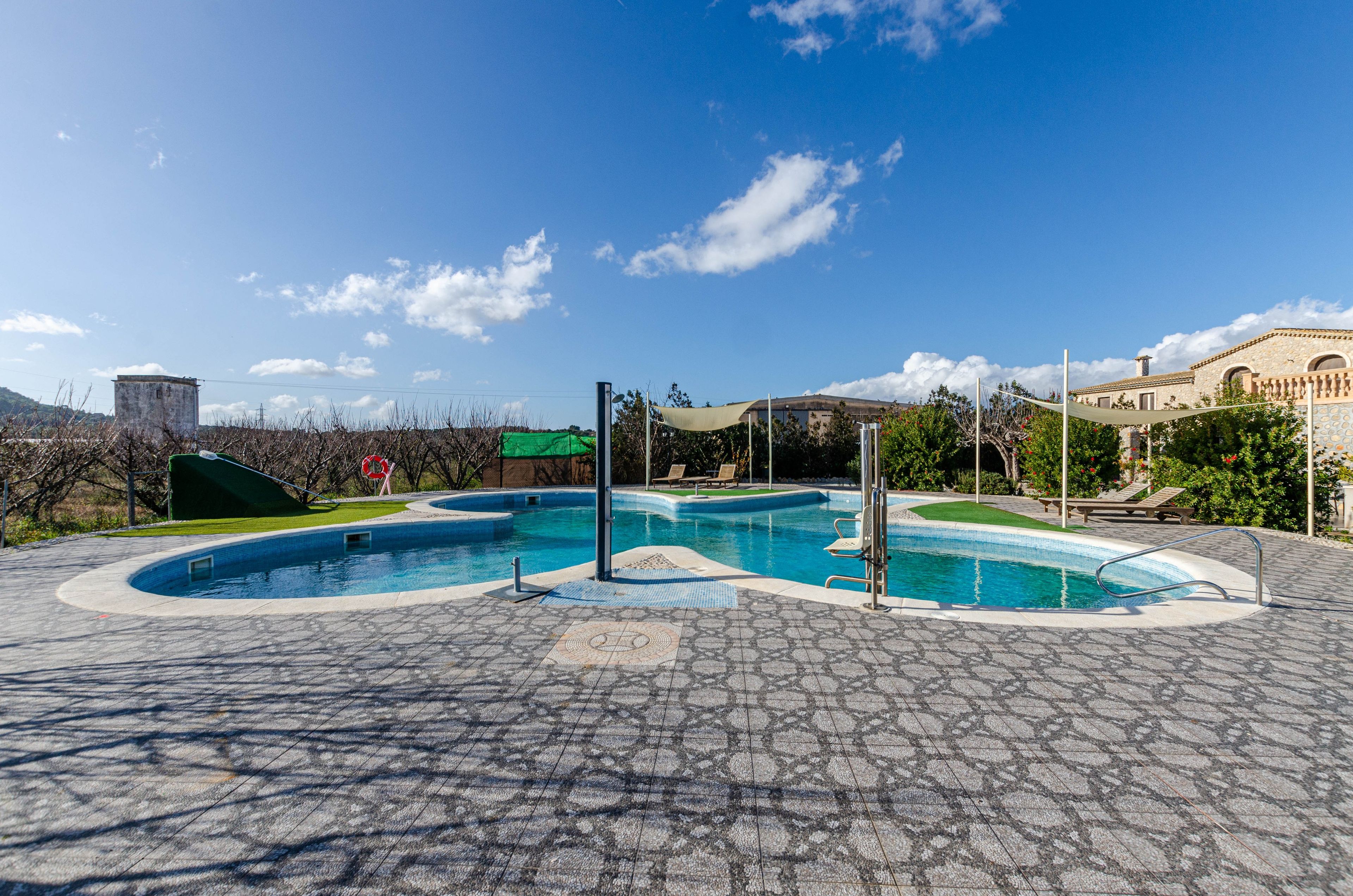 Una piscina con un diseño curvo único, rodeada por una zona pavimentada con suelo de baldosas estampadas.