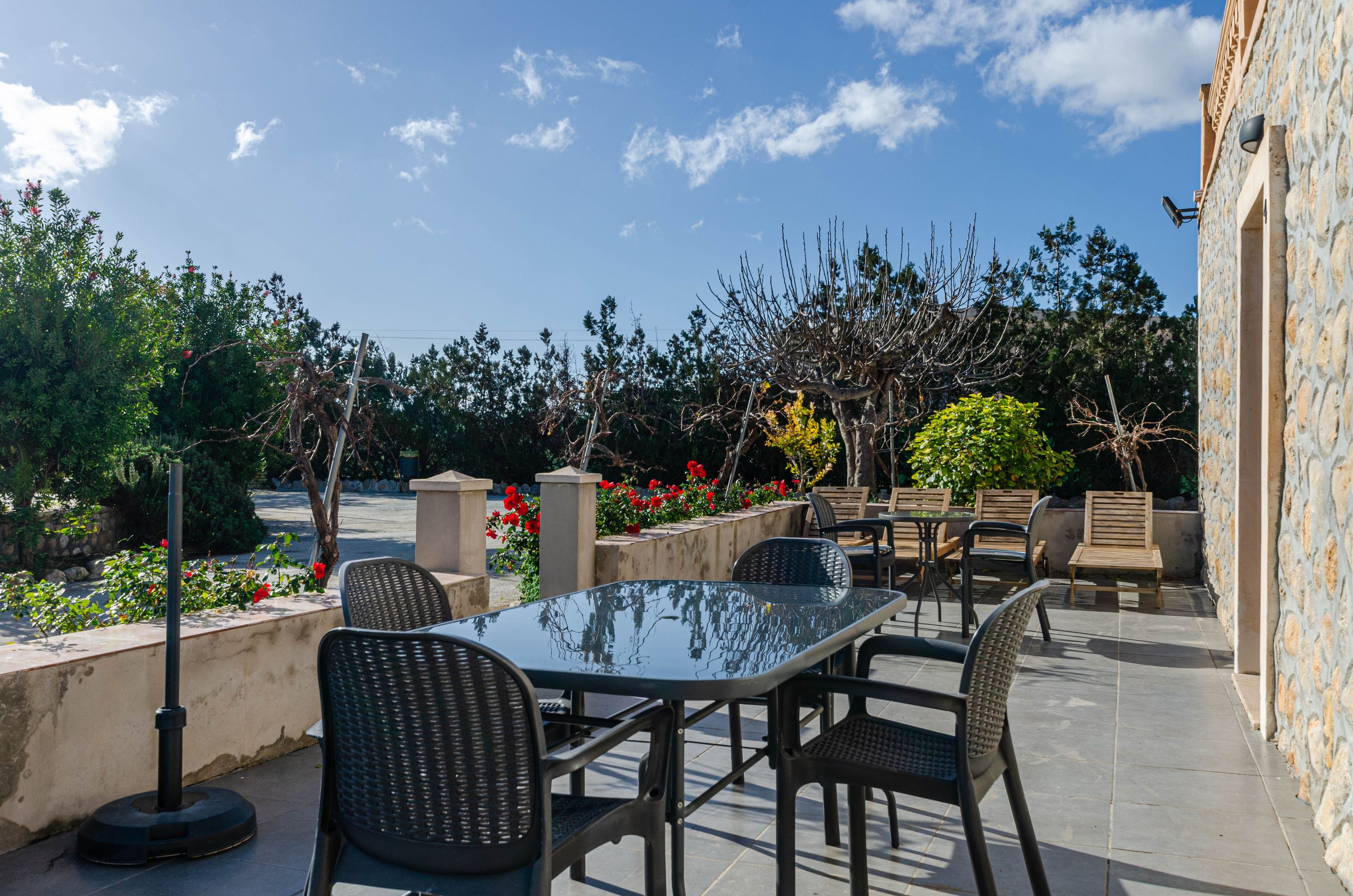 Un patio al aire libre con mesa y sillas, rodeado de muros de piedra y diversas plantas.
