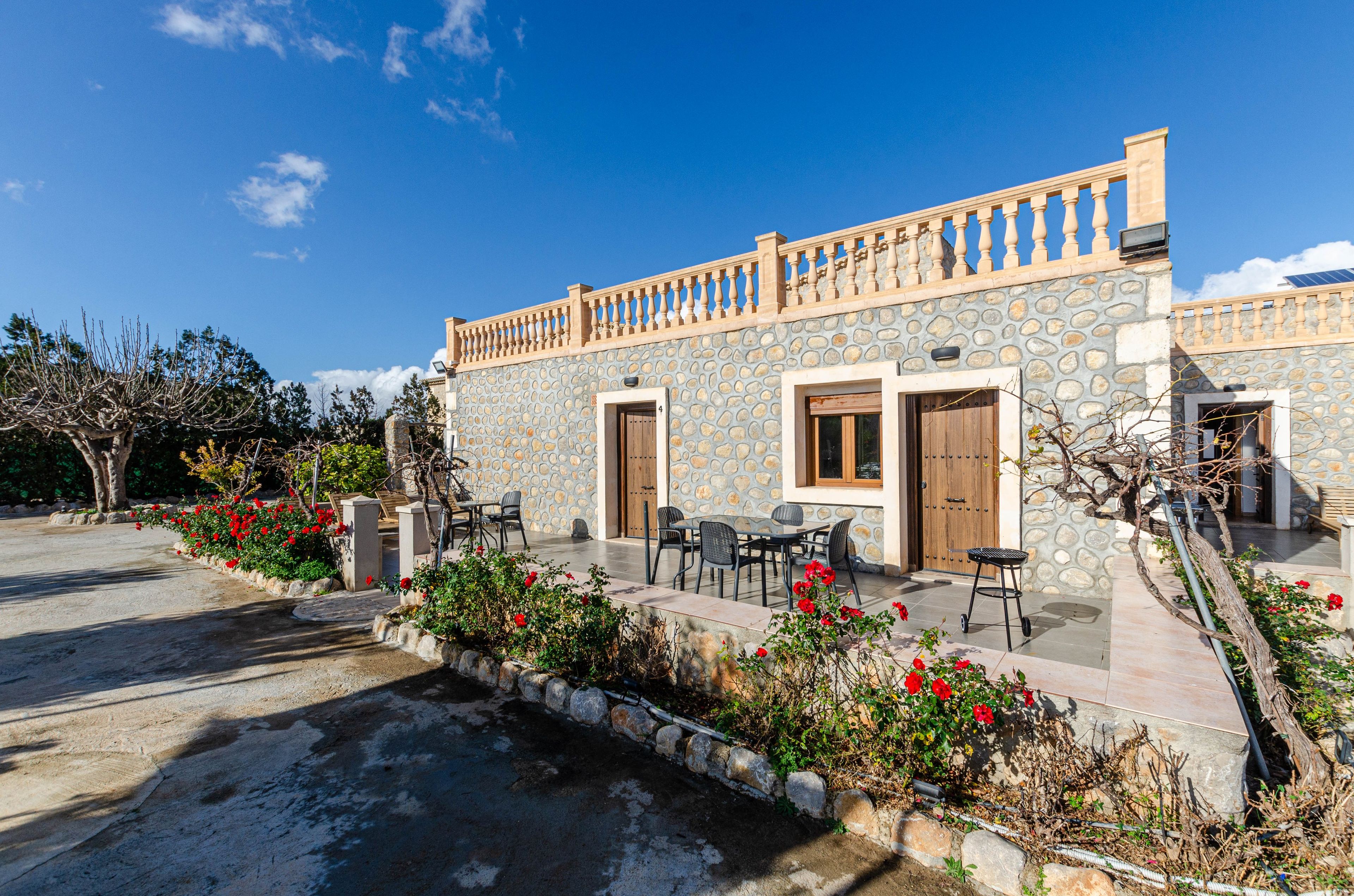 A stone building with a balcony, outdoor seating, and a garden with red flowers.
