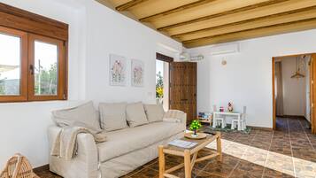A living room with a sofa, a coffee table, and a window. There is a door leading to another room.