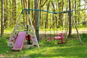 A playground with a slide and swings in a wooded area. - Waterfront 3-bedroom cottage with hot tub and AC (Gravenhurst)
