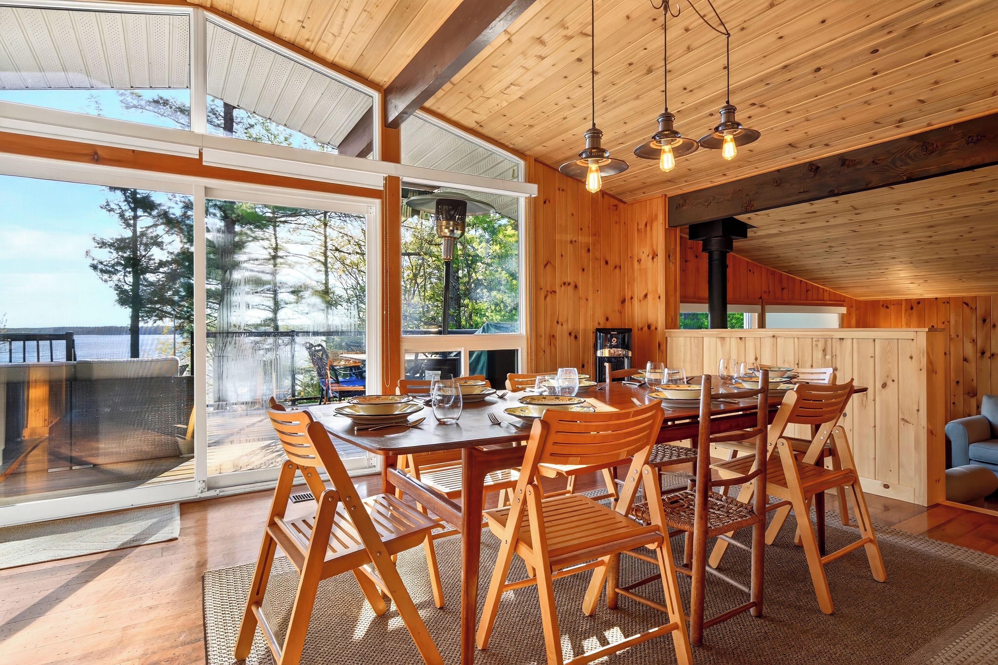 Un espace repas avec une table et des chaises en bois, de grandes fenêtres et une vue sur les arbres.