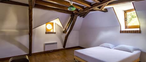 Un dormitorio con techo de madera, una cama, una silla, un ventanal y un calefactor fijado a la pared.