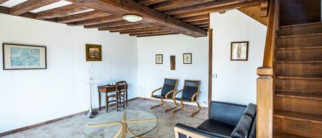 Une pièce avec un plafond en bois, une table en verre, deux chaises, un canapé et un escalier.