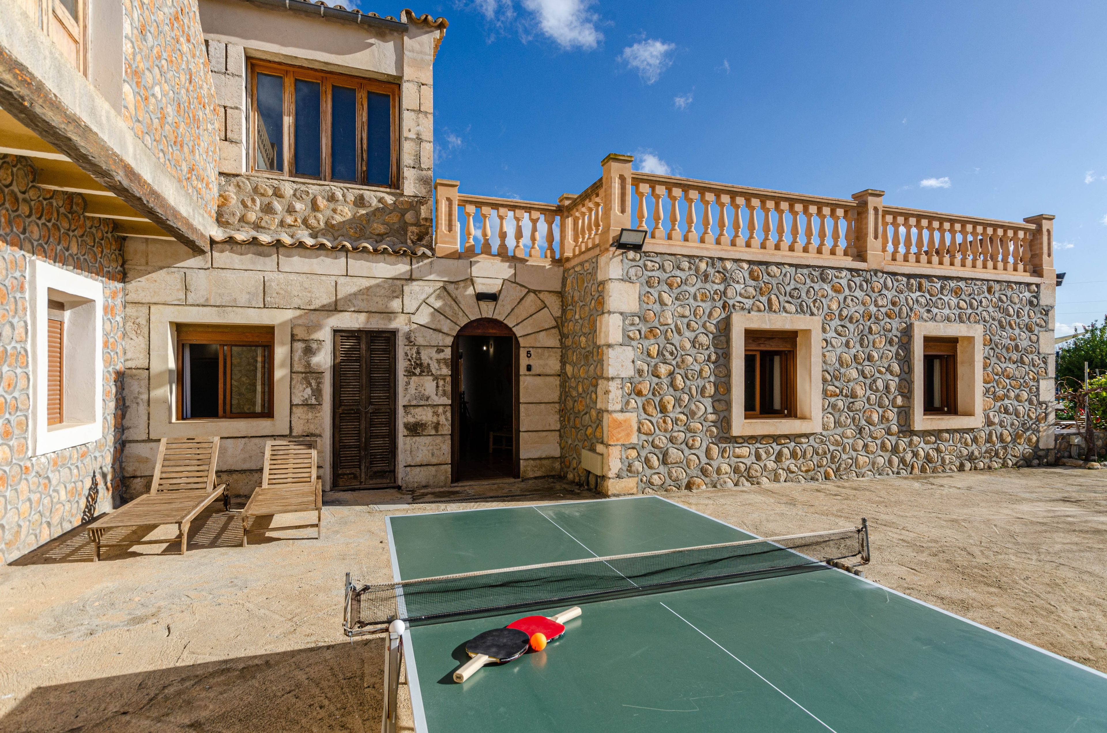 A courtyard with a tennis court, stone walls, and a wooden balcony.