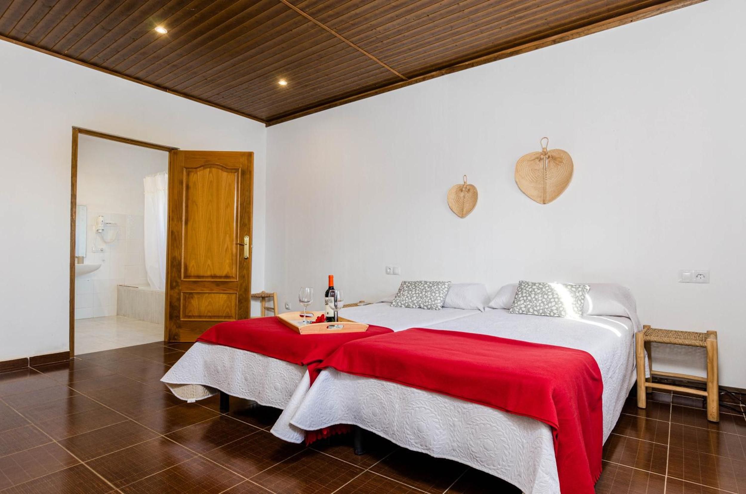 A hotel room with two beds, a wooden ceiling, a wooden door, and a small bedside table.