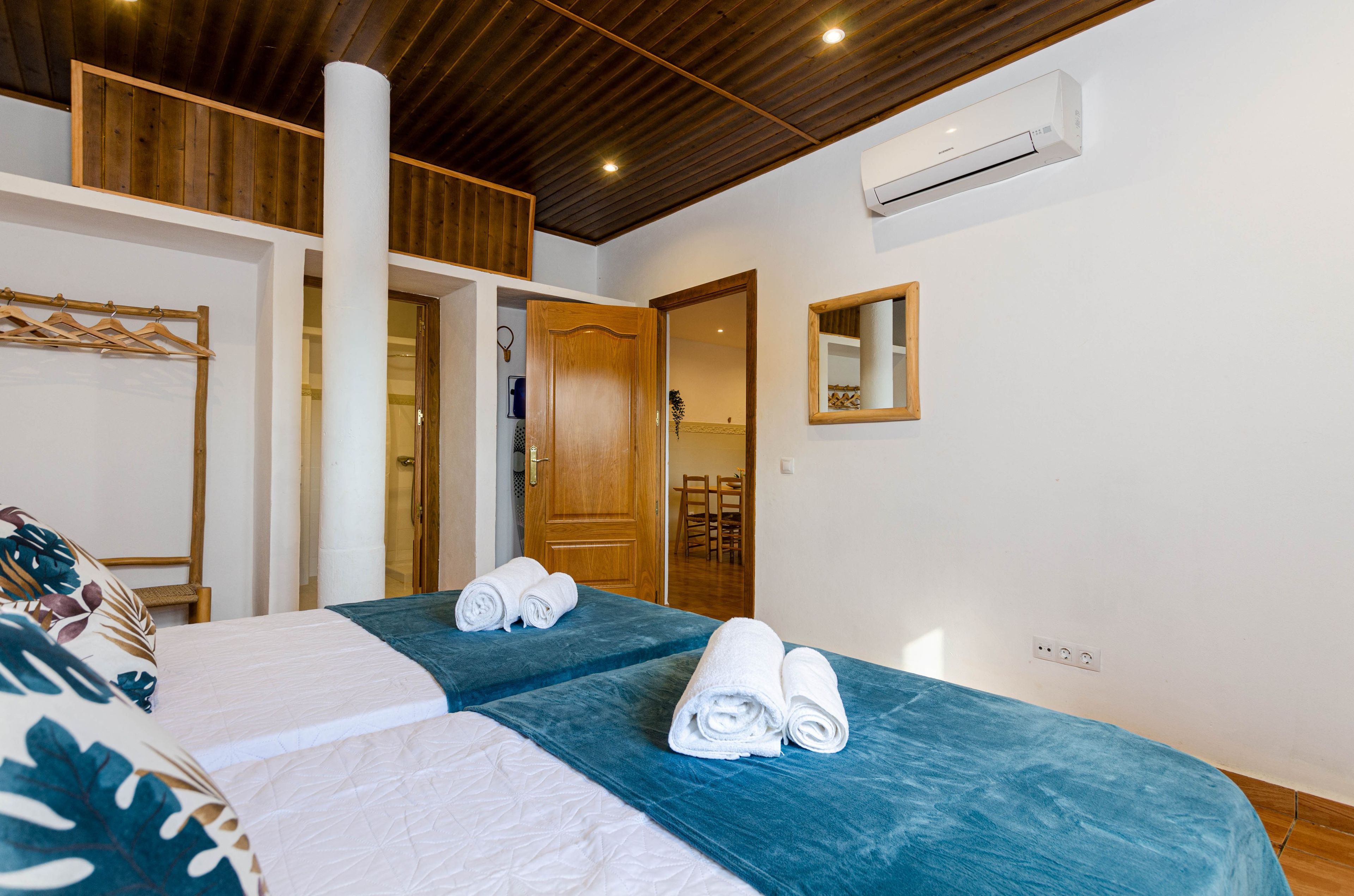 Habitación de hotel con dos camas, techo de madera, aire acondicionado, un espejo y una puerta de madera que da a otra habitación.