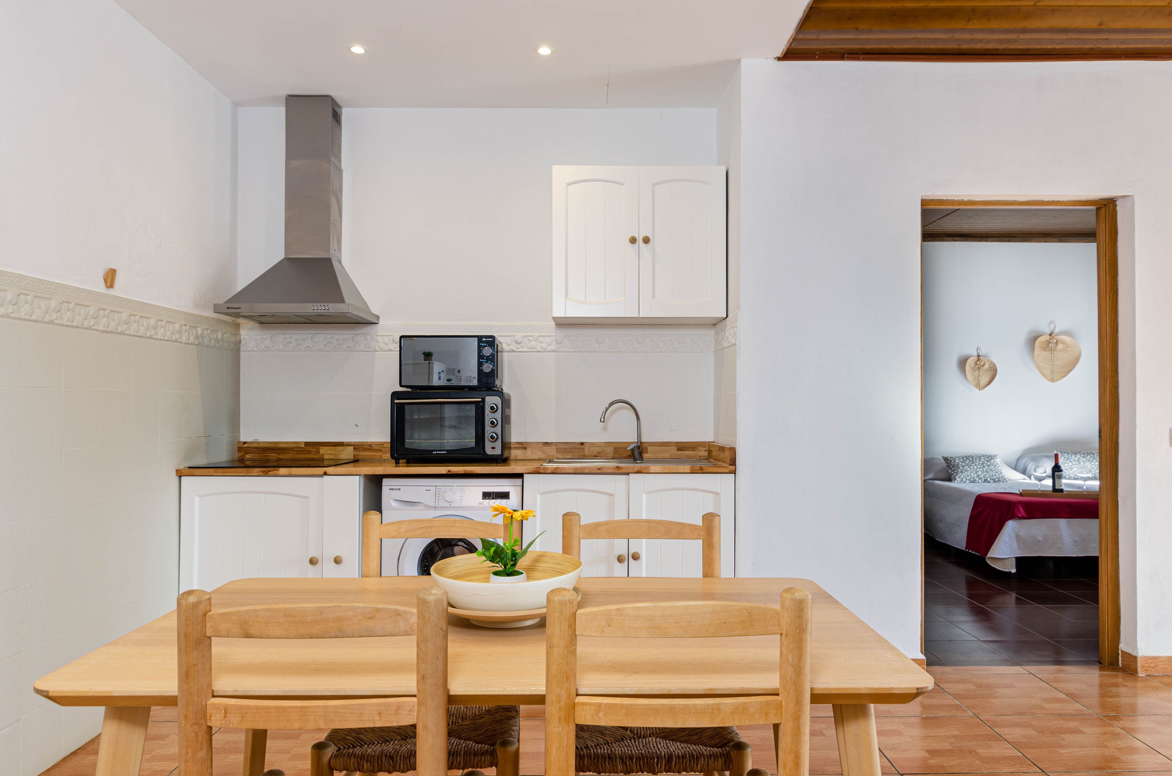 A compact kitchen with white cabinets, a microwave, and a stove. There is a dining table with chairs and a vase with flowers.