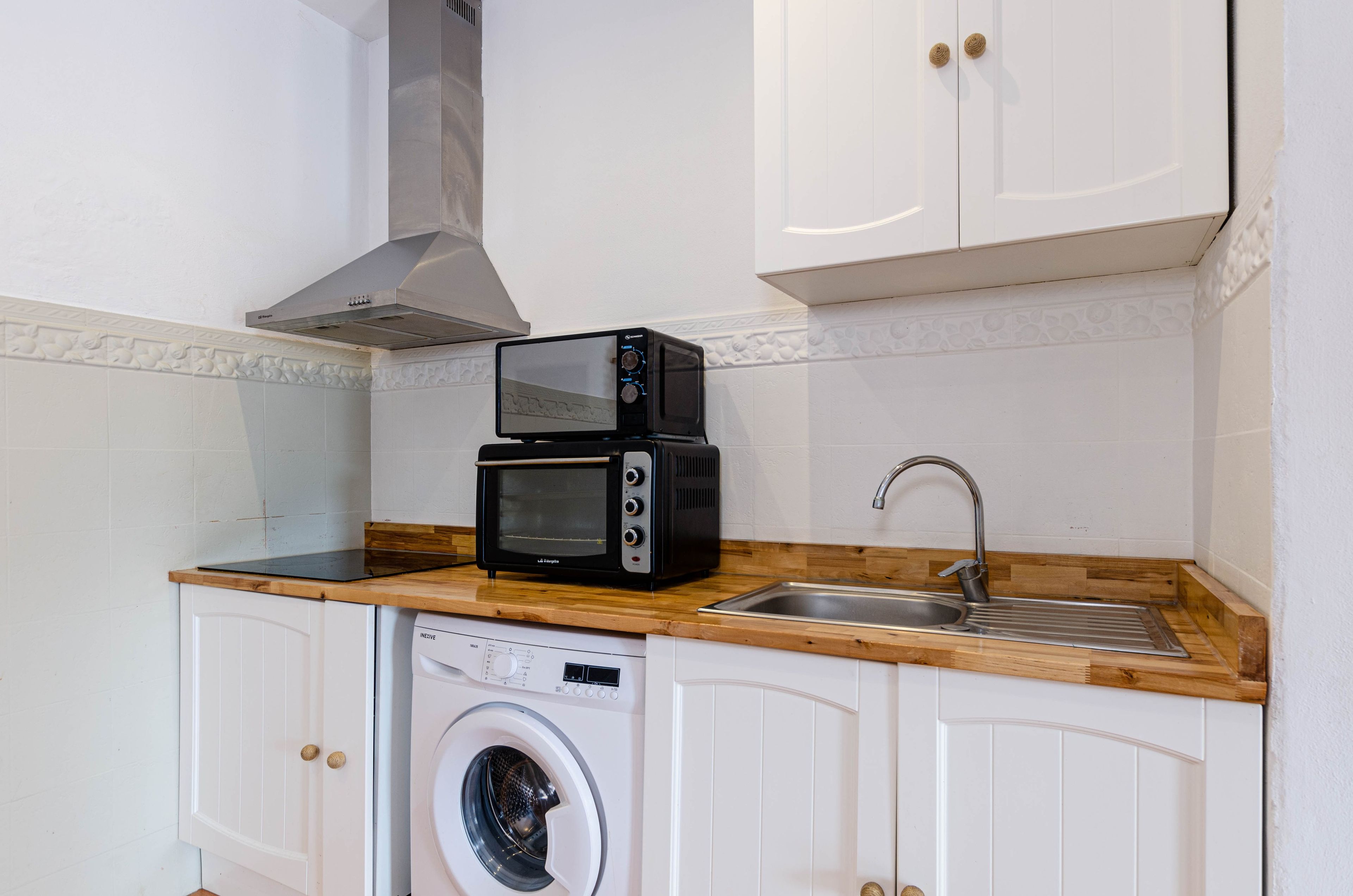Una cocina compacta con microondas, tostadora, lavabo y lavadora.