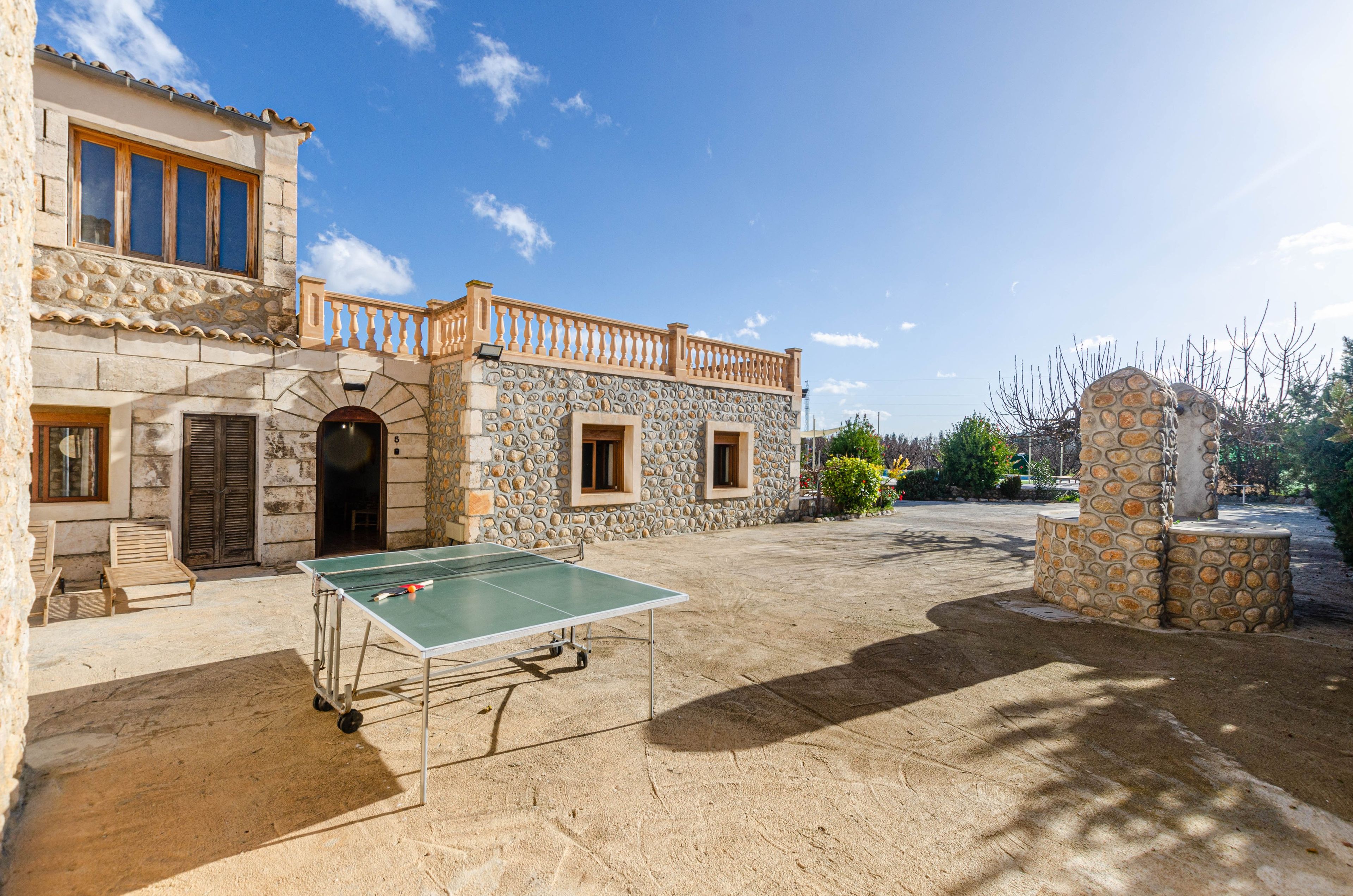 A courtyard with a ping pong table, stone walls, and a balcony.