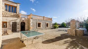A courtyard with a ping pong table, stone walls, and a balcony.