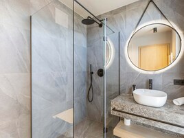 Un baño moderno con ducha envuelta en vidrio, un espejo redondo y encimera de mármol.