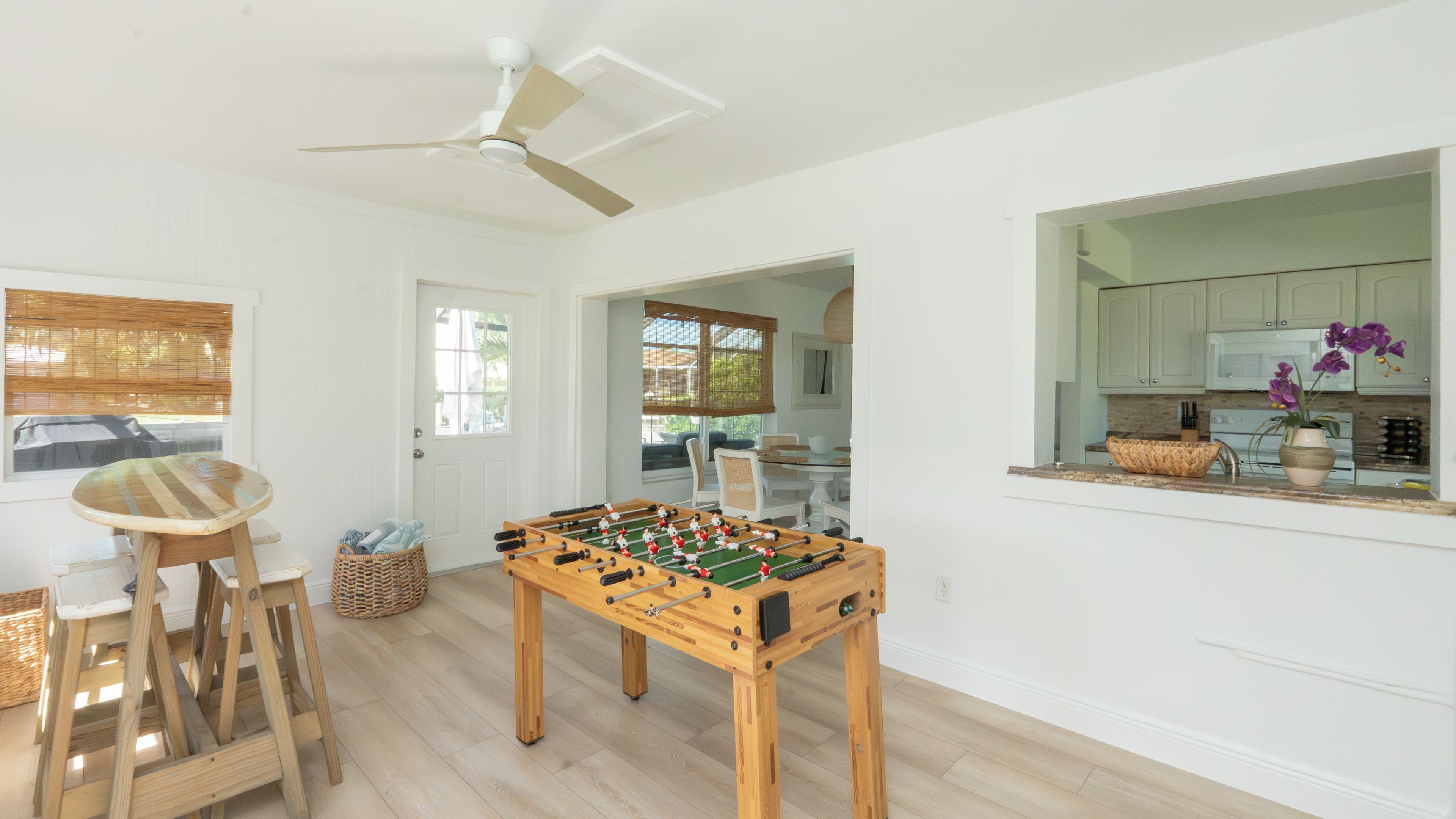 A room with a foosball table, a ceiling fan, and a view into a kitchen area.