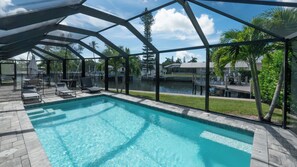 A swimming pool with lounge chairs and a view of a body of water. - Beautiful 3-bedroom, 2-bathroom waterfront home sits right on the canal! 1131 Fern Court (Marco Island)