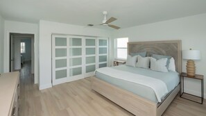 A bedroom with a bed, a nightstand, a lamp, a ceiling fan, and a walk-in closet with frosted glass doors. - Beautiful 3-bedroom, 2-bathroom waterfront home sits right on the canal! 1131 Fern Court (Marco Island)