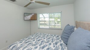A bedroom with a bed, a ceiling fan, a window with blinds, and a wall-mounted TV. - Beautiful 3-bedroom, 2-bathroom waterfront home sits right on the canal! 1131 Fern Court (Marco Island)
