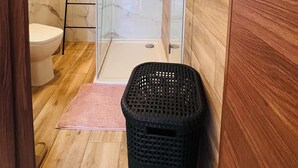 A bathroom with a glass shower enclosure, a wooden floor, a black trash bin, and a white toilet. - St. Julian's Central Apartment 5 (St. Julian's)