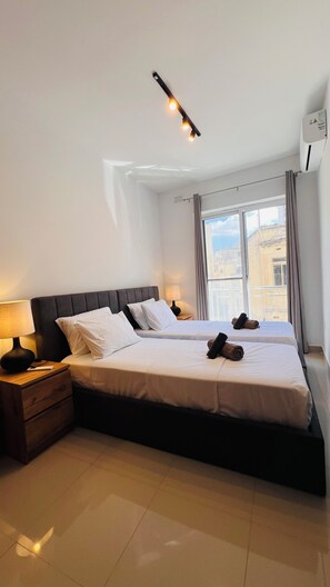 Ein Hotelzimmer mit einem großen Bett, einem Nachttisch mit Lampe, einem Fenster mit Vorhängen und einer Klimaanlage.
