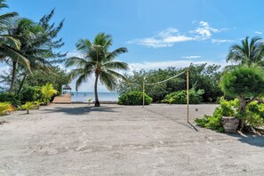 Ein Beachvolleyballfeld mit Netz, umgeben von Palmen und einer Holzpromenade, die zum Strand führt.