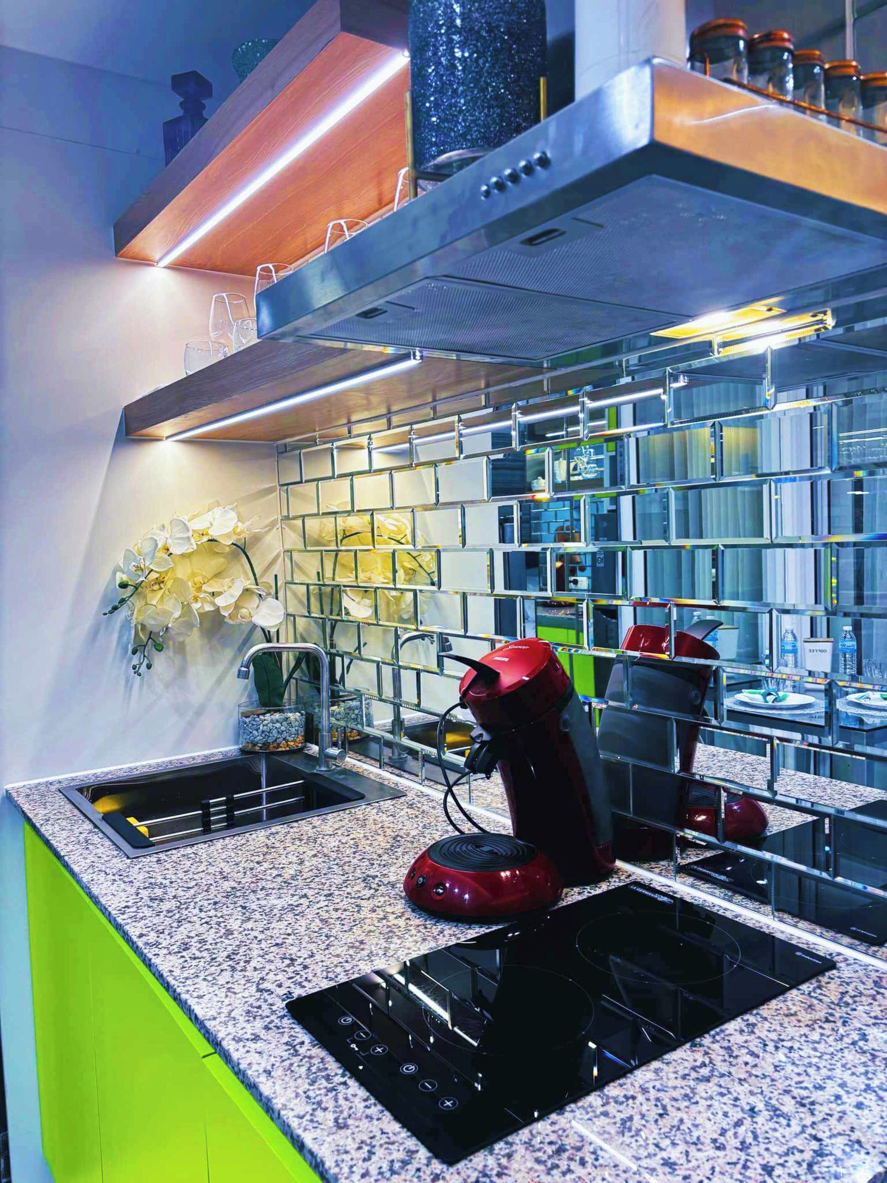 A modern kitchen with a granite countertop, a red coffee machine, and a stainless steel range hood.