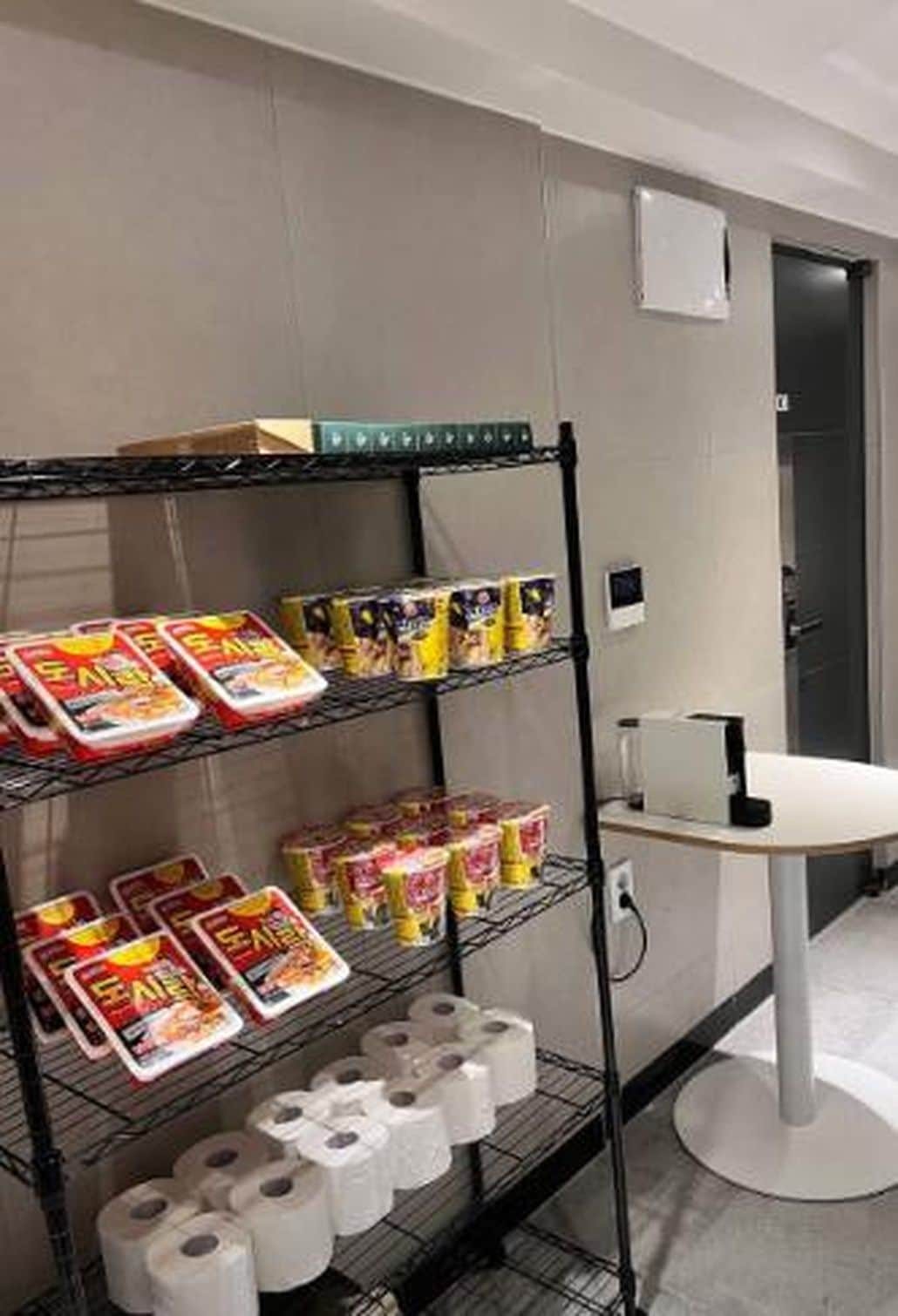 A shelf with toilet paper and paper towels, a white table, and a door in the background.
