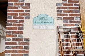 Ein Schild für das Chateau de la Grange Arthuis, darunter der Name 'Les Douves', angebracht an einer Ziegelwand.