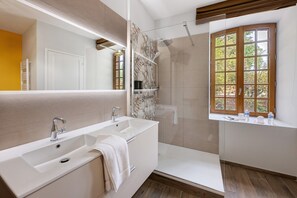 Ein modernes Badezimmer mit einem großen Spiegel, einer Badewanne, einer Dusche und einem Fenster mit Blick auf Bäume.
