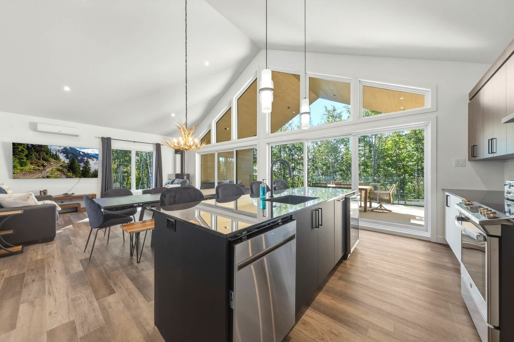A modern kitchen with a central island, large windows, and a dining area with a view of the outdoors.