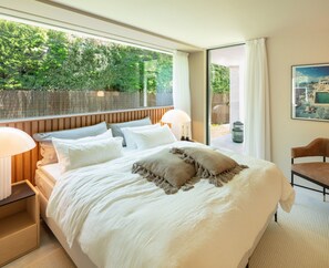 Ein Schlafzimmer mit einem großen Bett, zwei Nachttischlampen, Blick ins Grüne und einem gerahmten Bild an der Wand.