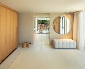 Ein modernes Interieur mit einem großen Holzschrank, einem runden Spiegel, einer gepolsterten Bank und Blick in einen hellen Raum mit Holzlattenzaun.