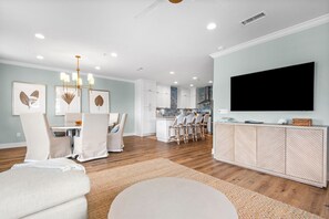 A modern living room with a dining area, kitchen, and a large TV mounted on the wall. - Pet-Friendly 3BR Penthouse Seagrove Beach | Private Beach Access & Pool (Santa Rosa Beach)