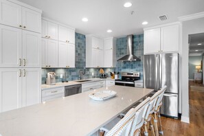A modern kitchen with white cabinetry, a stainless steel refrigerator, and a central island with bar stools. - Pet-Friendly 3BR Penthouse Seagrove Beach | Private Beach Access & Pool (Santa Rosa Beach)