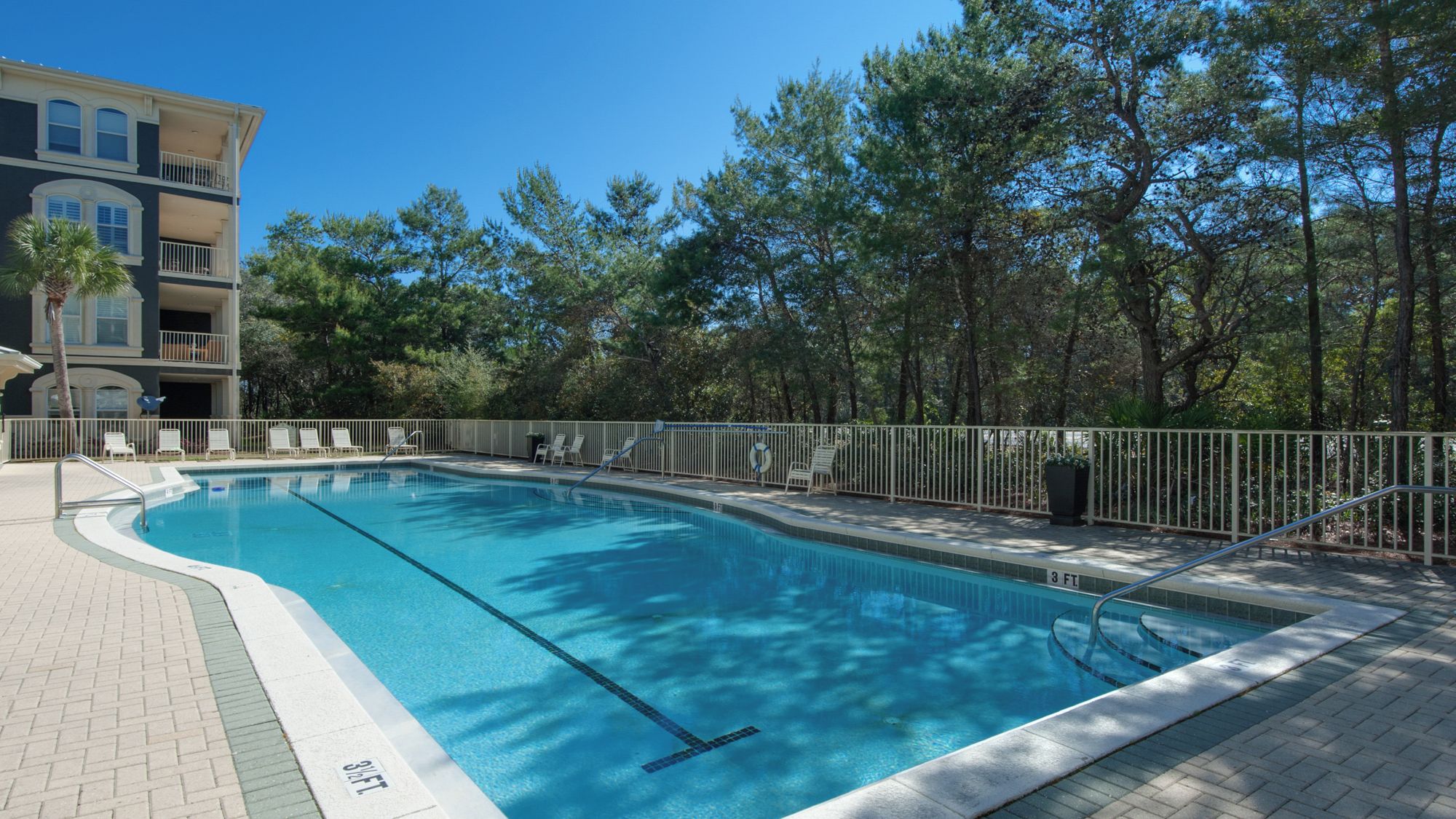 A swimming pool with a surrounding fence, a lifeguard stand, and lounge chairs.
