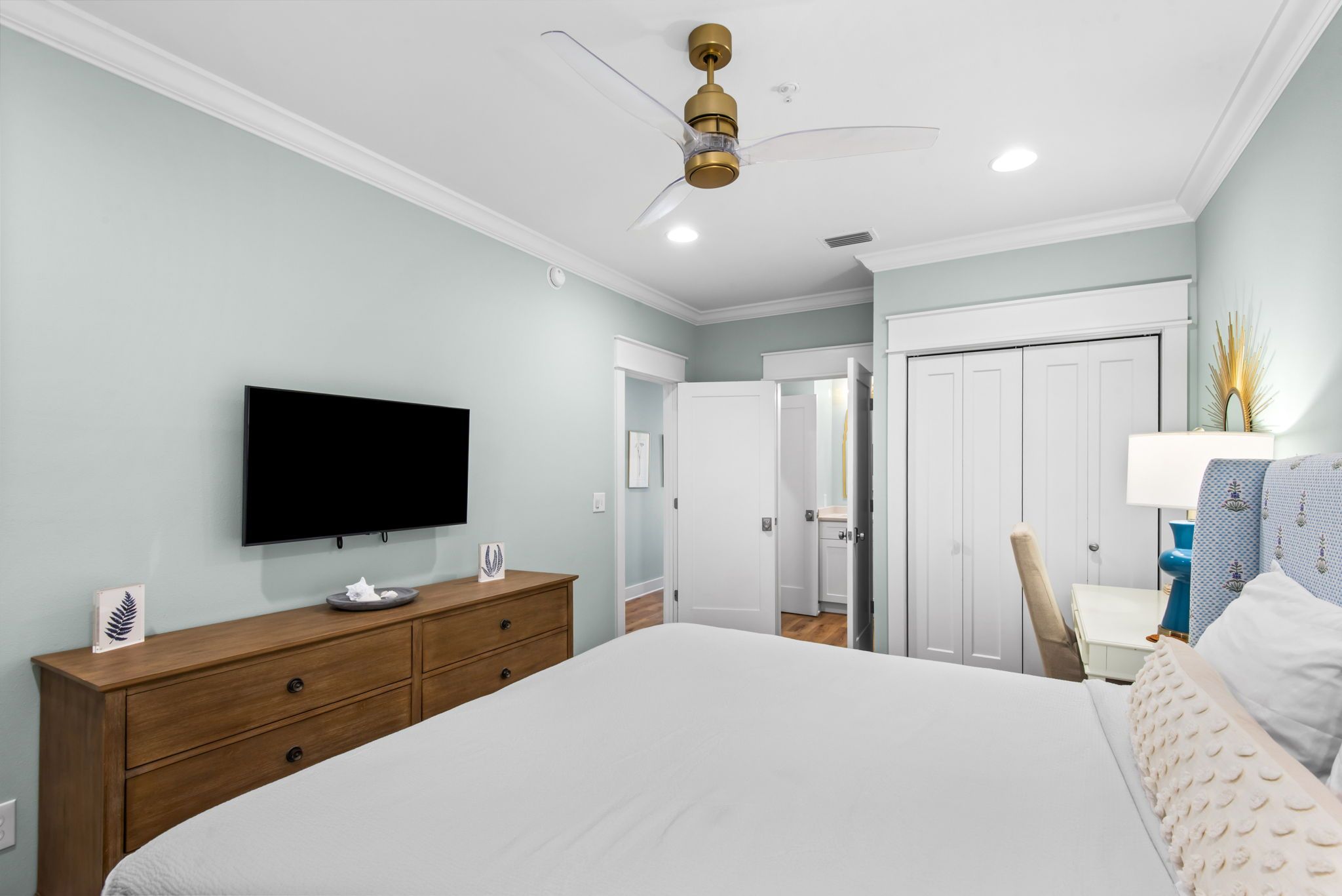 Ein Schlafzimmer mit Bett, Fernseher, einem hölzernen Schminktisch, Deckenventilator und Kleiderschrank.