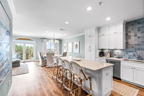 A modern kitchen with white cabinetry, a central island with bar stools, and a dining area with a view to the outdoors. - Pet-Friendly 3BR Penthouse Seagrove Beach | Private Beach Access & Pool (Santa Rosa Beach)