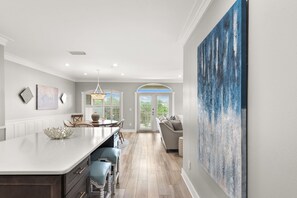 A modern kitchen with a central island, dining area with chairs, and a large abstract painting on the wall. - 3BR Seagrove Beach Pet-Friendly Penthouse | Private Beach & Pool (Santa Rosa Beach)