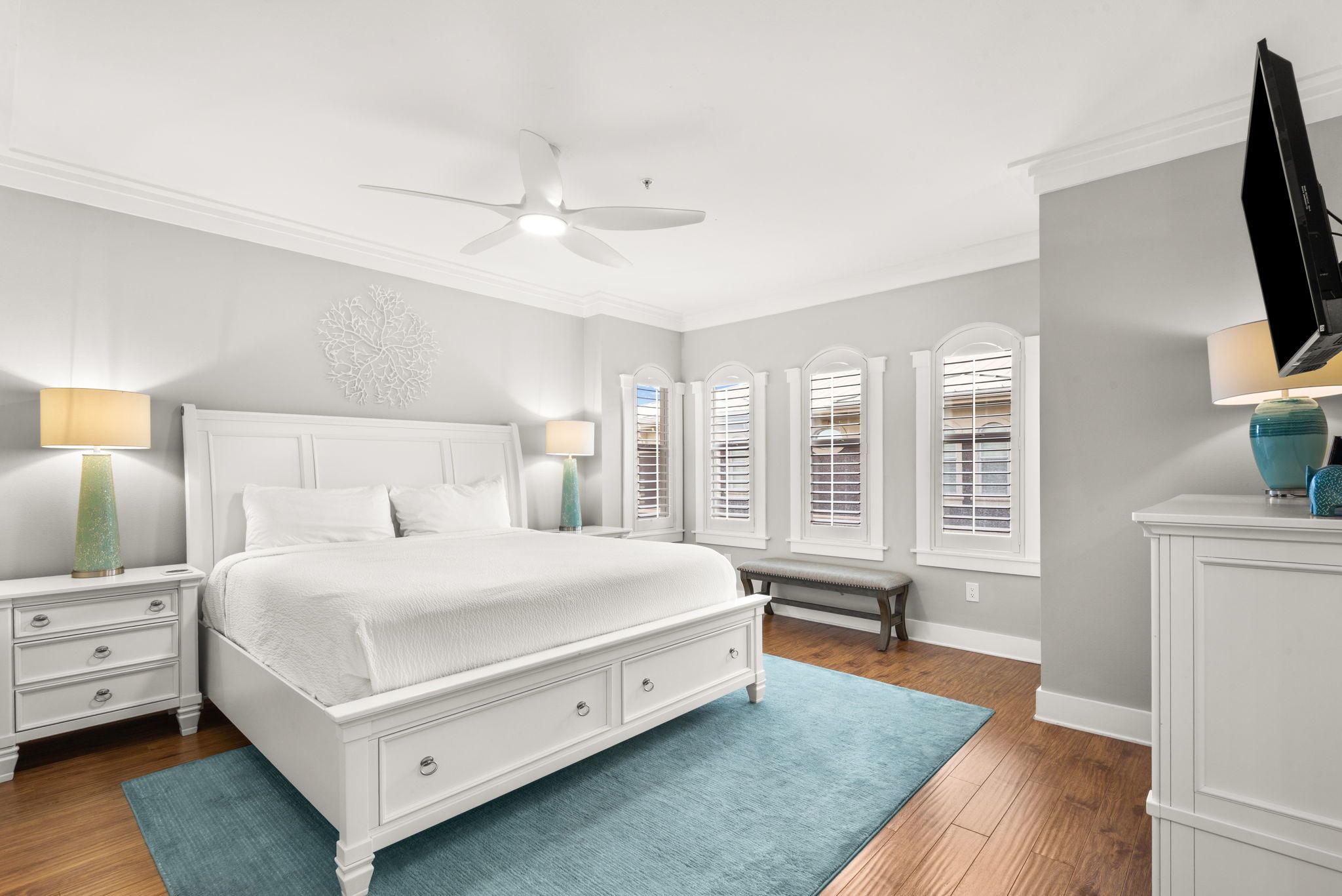 Une chambre à coucher comprenant un lit, des tables de chevet, un banc, une commode et un ventilateur de plafond.