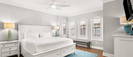 Une chambre à coucher comprenant un lit, des tables de chevet, un banc, une commode et un ventilateur de plafond.