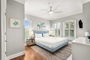 Ein Schlafzimmer mit einem Bett, Nachttischen, einem Deckenventilator und einem Fenster mit Fensterläden.