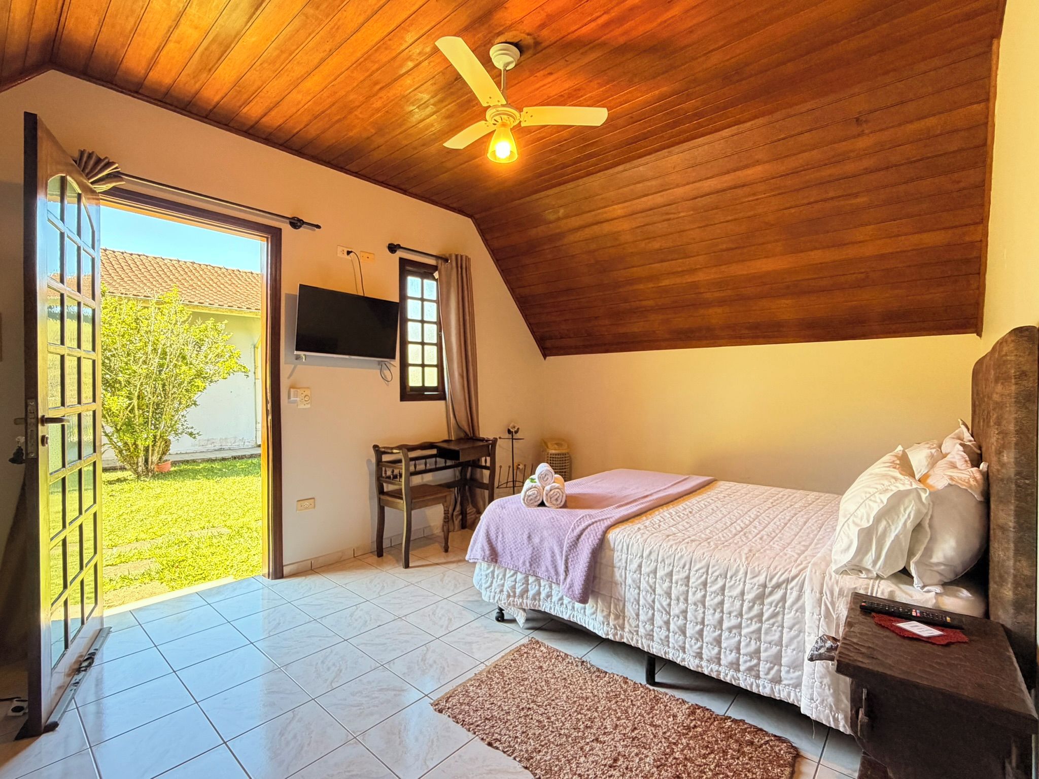 Un dormitorio con una cama, un escritorio, un televisor y un ventilador de techo.