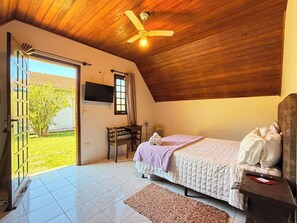 A bedroom with a bed, a desk, a television, and a ceiling fan.