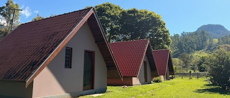 Una hilera de edificios sencillos de una sola planta con techos rojos, ubicados en un área con césped, árboles y una colina al fondo.