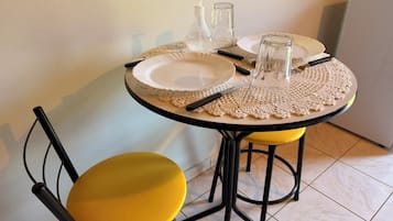 A round dining table with a white plate, two glass bottles, and a glass. There are two yellow chairs with black frames.